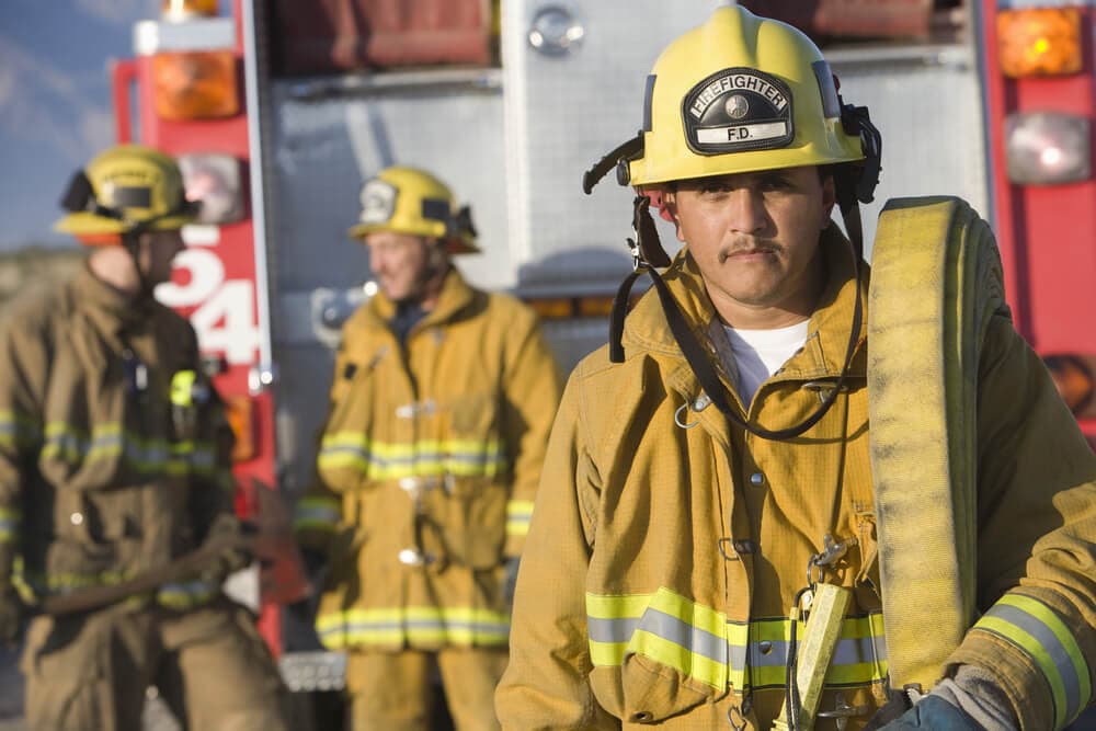 Three firefighters in gear in front of fire truck