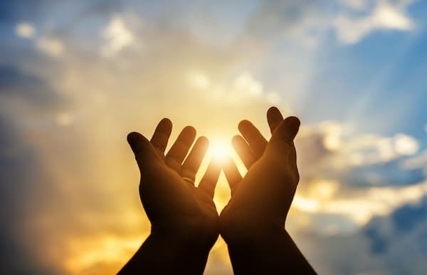 Hands reaching out in prayer toward sun and clouds