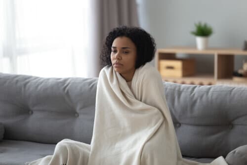 Sick young woman wrapped in a blanket and sitting on her couch.