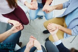 Aerial photo of group therapy with people sitting in a circle holding hands