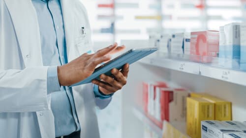 pharmacist holding a tablet in front of aisle with medications