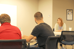 two men in foreground listening to Amy Woodward discussing to her message on parenting in recovery.